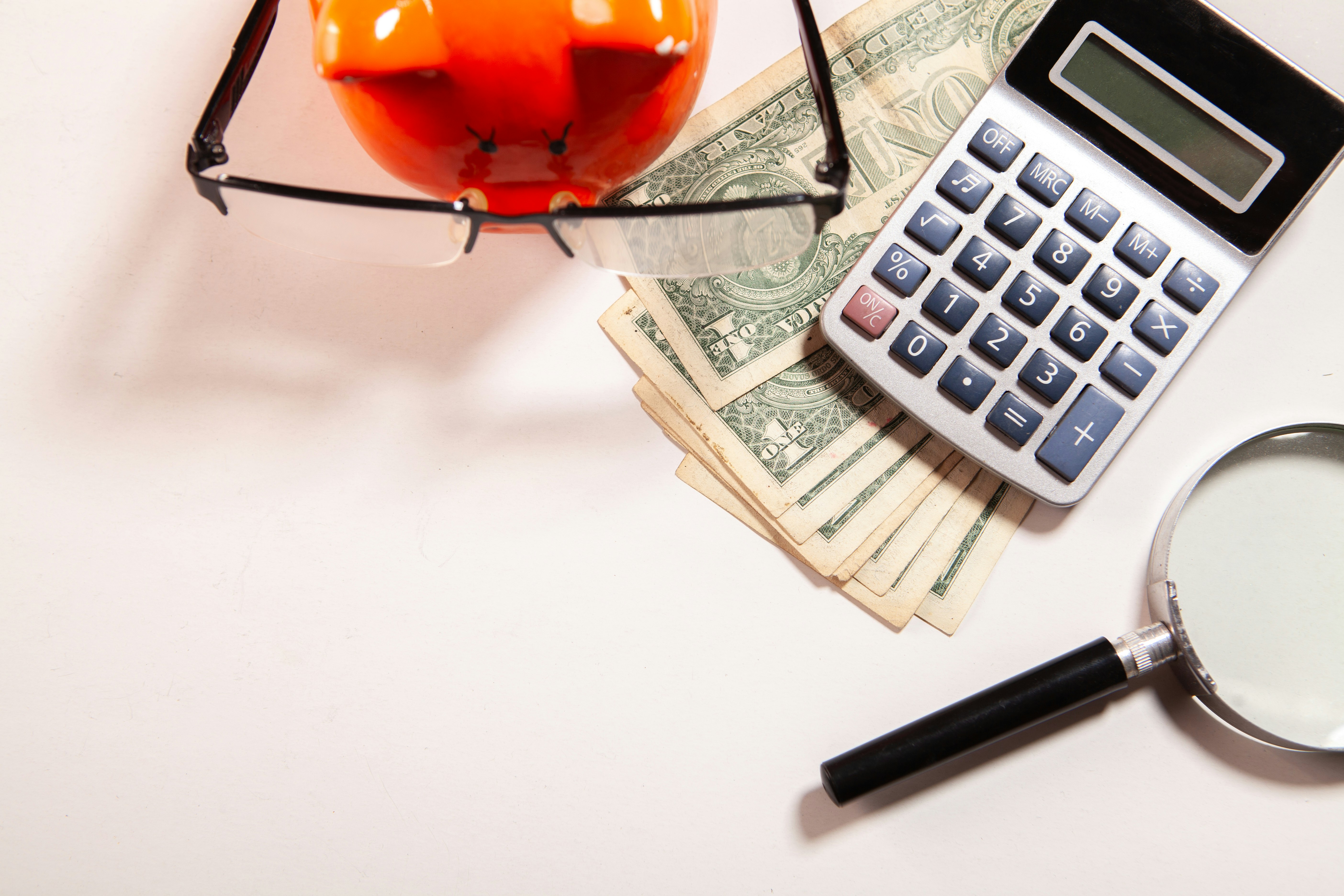 Piggy bank with dollars, calculator, and magnifying glass to represent allowable costs