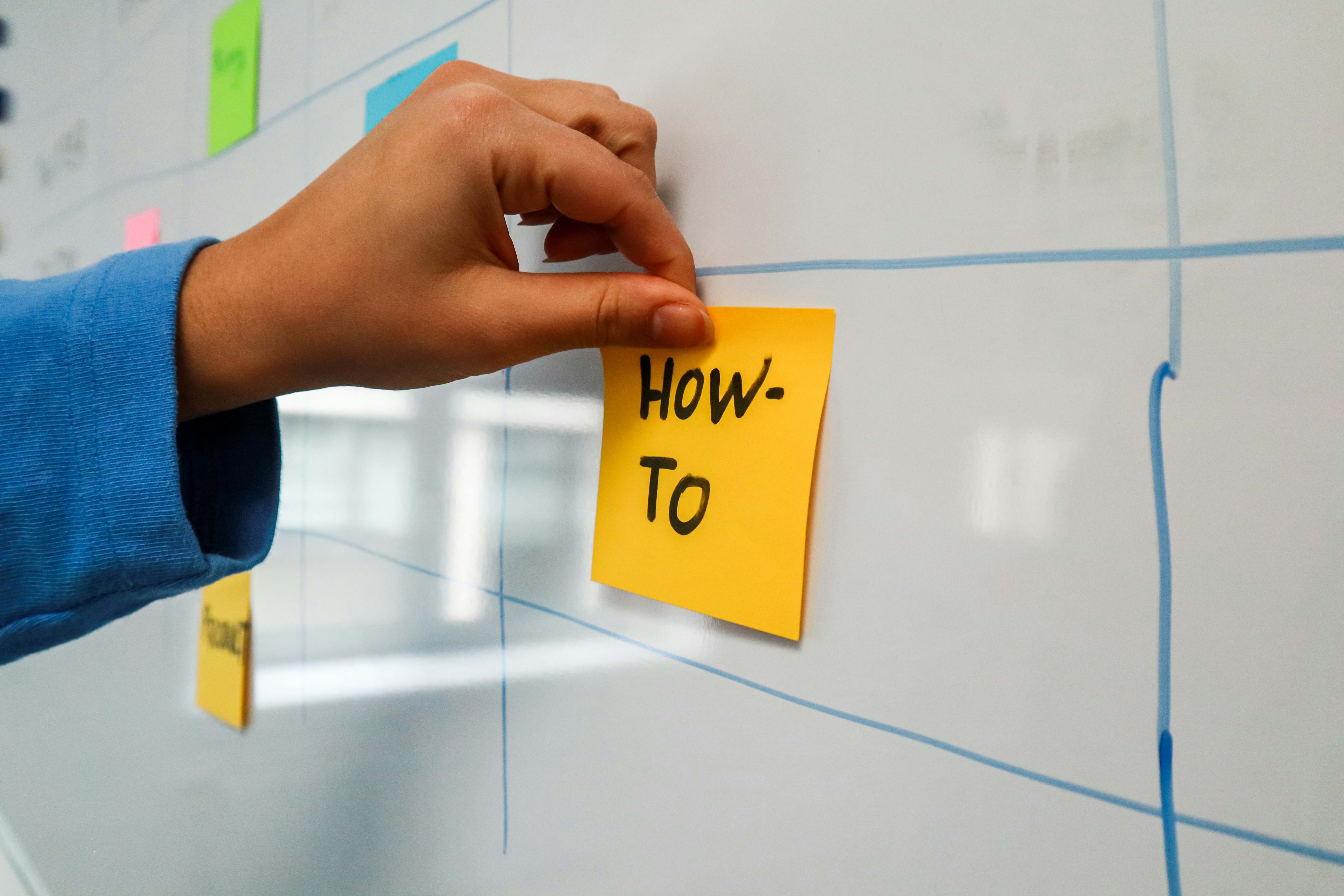 Person posting How To sticky note on a whiteboard.